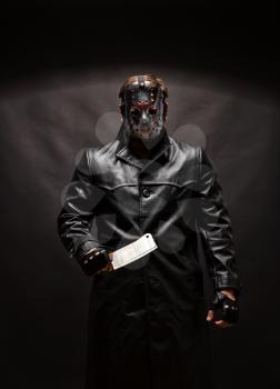 Portrait of bloody murderer in hockey mask holding a meat cleaver in hand against black background.