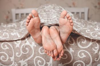Couple legs stick out from under a blanket in bedroom. Loving couple concept. 