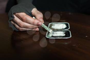 Rolled dollar in addict hands and dose of cocaine on mirror isolated on wooden background.