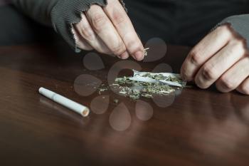 Addict hands making marijuana jamb closeup, wooden background.