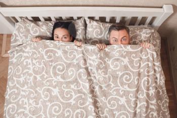Young couple peeping from bedsheet at bedroom.  Playfull moments of loving couple.