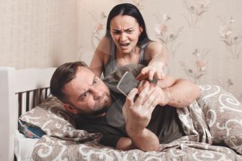 Wife irritate while husband using phone in bed. Couple quarrel concept.