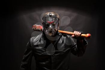 Psycho killer in hockey mask with bloody bat on black background.