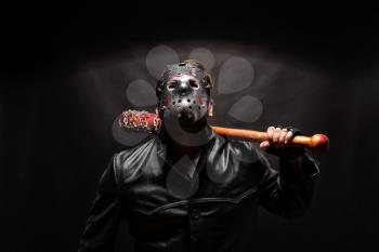 Bloody maniac in hockey mask and black leather coat with bat on black background