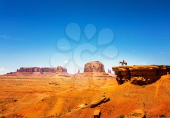 Cowboy on a horse on the top of sandstone mountain against blue sky at Monument Valley National Tribal Park, Navajo, Utah, USA