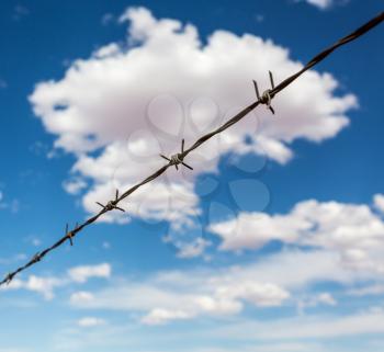 Barbed wire againdt deep blue cloudy sky. Contrast of freedom and conclusion