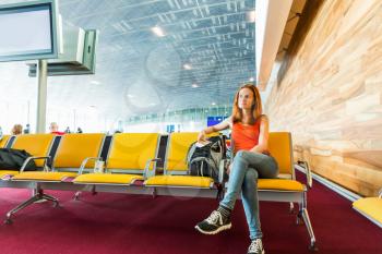 Young female traveller with ticket in her hands sitting on the chair in waiting hall. Suitable for bus, railway, metro station.