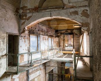 Old prison corridor with grunge rusty cells and metal staircase.