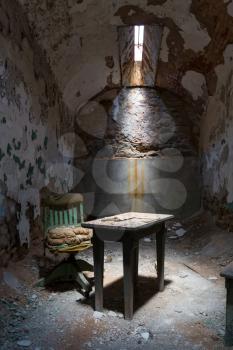 Old prison cell with little sunlight window, table and grunge chair.