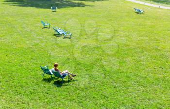 Woman sitting on armchair in the middle of the meadow. Meadow with green grass at sunny day.