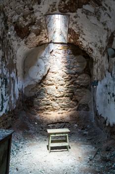 Old prison cell with little sunlight window, grunge chair.