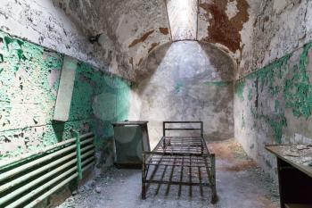 Grunge prison cell with metal bed and sunlight window