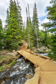 Wooden bridge through the mountain river against green forest.