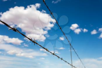 Barbed wire againdt deep blue cloudy sky. Contrast of freedom and conclusion