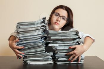 Tired female accountant hugs big stacks of documents