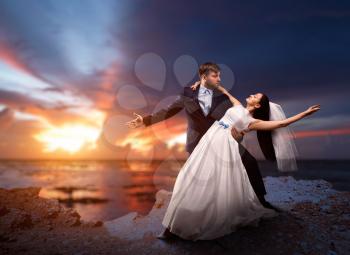 Droom and bride dancing on the background of the sea and sunset. Newlyweds in love