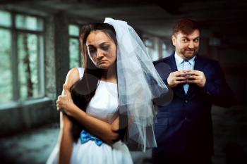 Bride with tearful face, groom with sly smile on background. Unhappy marriage
