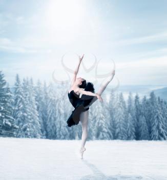 Graceful female ballet dancer stretching, winter snowy forest on background