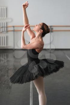 Skill ballerina posing in ballet class, barrre and white wall on background