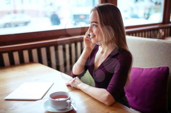 Businesswoman talking by smartphone in coffee shop.