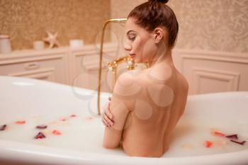 Beautiful nude woman in bathtub with rose petals and foam.