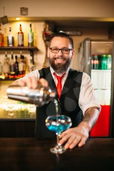 Bartender with shaker making alcohol cocktail behind a bar counter