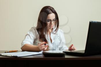 Young female bookkeeper in glasses using laptop in office