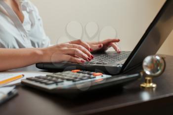 Female accountant hands on keyboard, calculator, laptop and accounting documents on the table closeup.