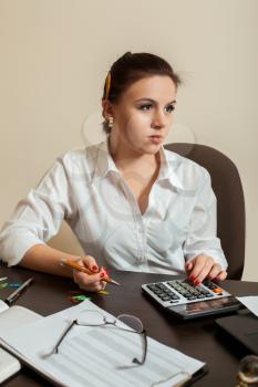 Young woman bookkeeper considers on the calculator, chancellery on wooden table