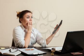 Scared female bookkeper looks at the accounting balance sheet.