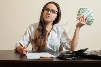 Female bookkeeper holding dollars fan in her hand. Business woman with money in hand signs financial documents