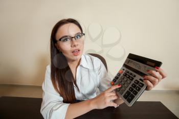 Smiling young female bookkeeper with calculator and accounting documents has reduced balance