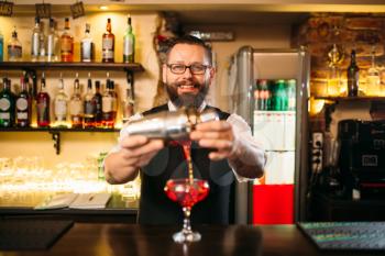 Barman is making alcohol cocktail at bar counter. Barman with shaker and glass of beverage