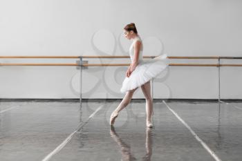Beautiful female ballet dancer in ballet class, barre and white wall on background