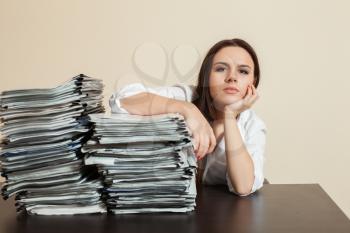 Young female accountant hugs big stacks of documents. Office on background