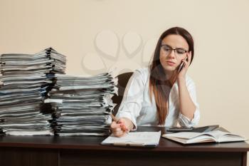 Female accountant manager talking by phone, stacks of documents on the table.