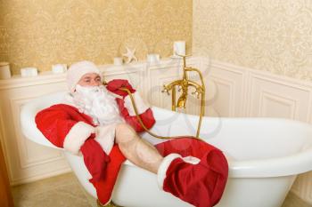 Funny drunk Father Christmas lies in a bath and talking by shower.