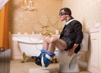 Man in pilot glasses sitting on the toilet bowl. Bathroom interior in retro style on background
