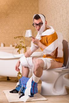 Man in glasses wrapped in toilet paper sitting on the bowl. Bathroom interior in vintage style on background