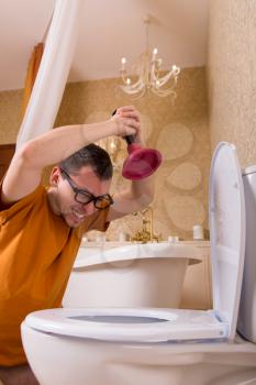 Man in glasses clears the clog in the toilet. Luxury bathroom interior on background