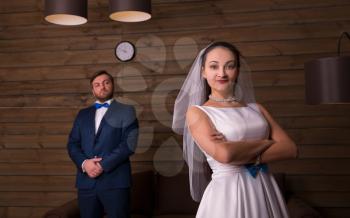Young bride and serious groom on photo shoot, wooden room on background.