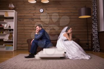 Portrait of unhappy family couple sitting on the table, wooden room on background.