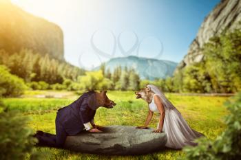 Bride and groom with wild animal heads, mountains and green forest on background.