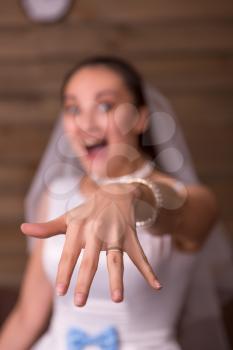 Bride in white dress and veil showing golden wedding ring on her hand, wooden room interior on background