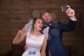 Smiling bride and groom making selfie on mobile phone, wooden background.
