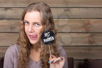 Cute girl holding funny icon on a stick with  just married inscription, wooden background. Fun photo props and accessories for shoots