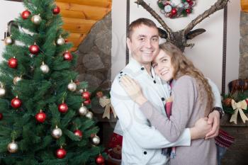 Portrait of love pair standing near christmas tree decorated with colorful balls