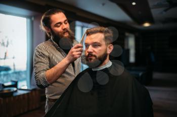 Barber combing hair of the client man in salon cape. Barbershop concept