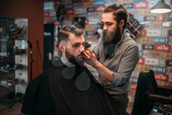 Coiffeur cutting hair of the client man in black salon cape. Barbershop concept