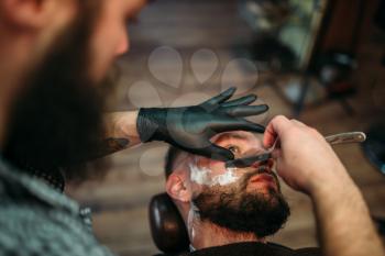 Barber shaves the beard of the client by straight razor at barbershop. 